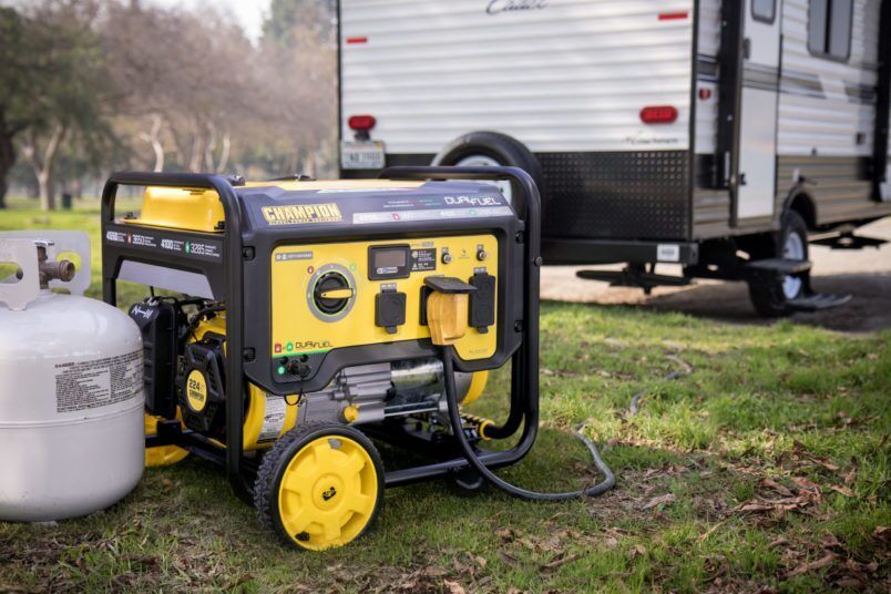 Yellow portable generator beside a white propane tank in a grassy campsite, with an RV in the background