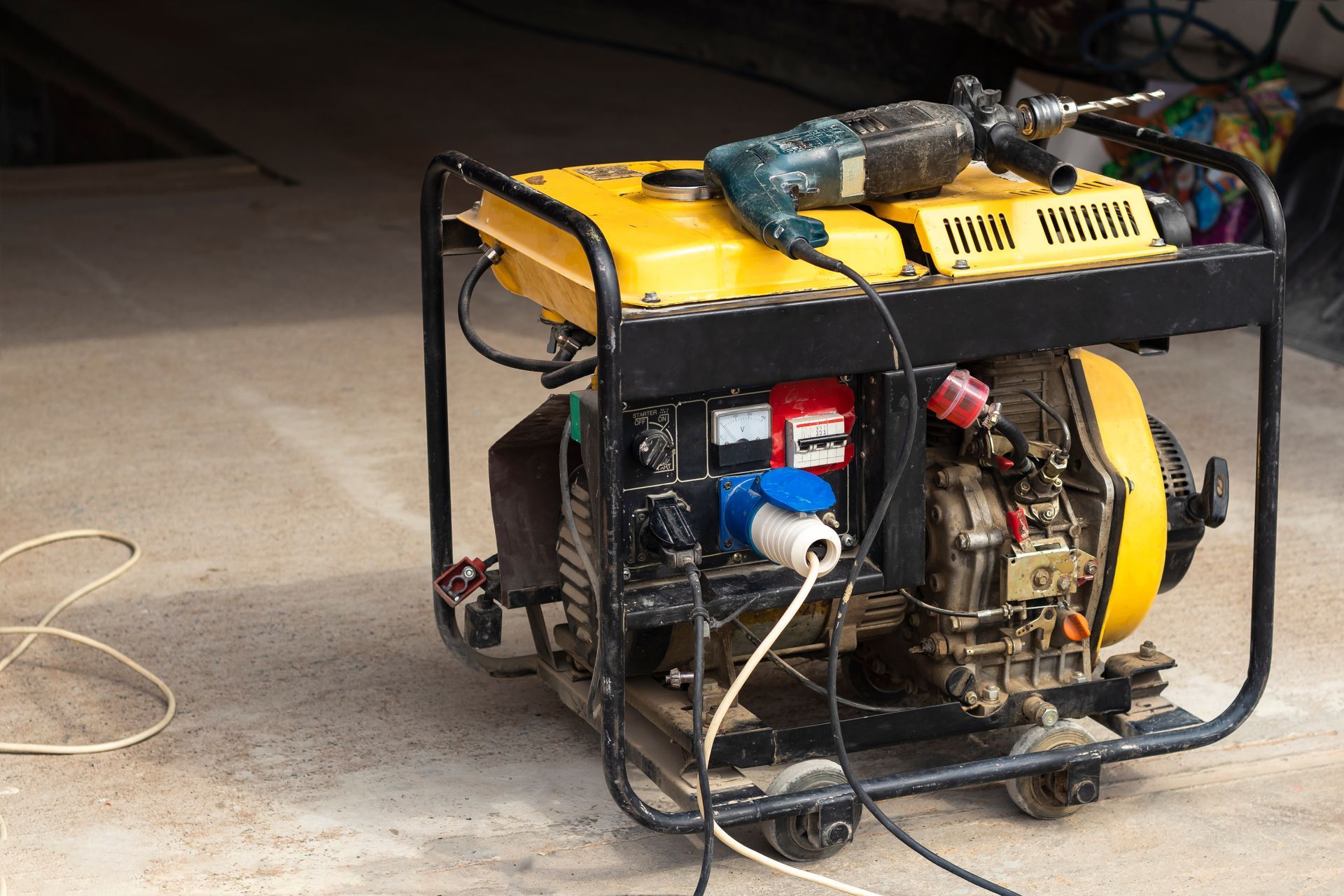 Portable generator in a black metal frame with a yellow top, sitting on a concrete floor with cables attached