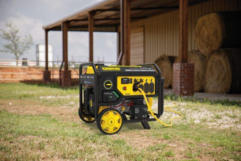 Yellow-and-black portable generator on grass beside a barn and hay bales