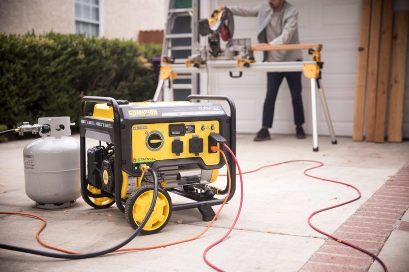 Portable generator beside a propane tank powering a table saw on a driveway during home renovation