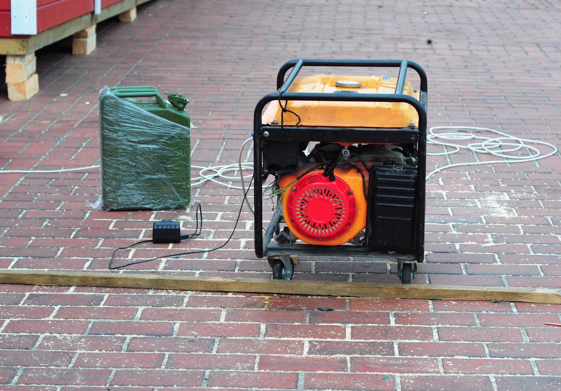 Two portable generators on a brick sidewalk, one wrapped in green plastic and one with a red front cover.