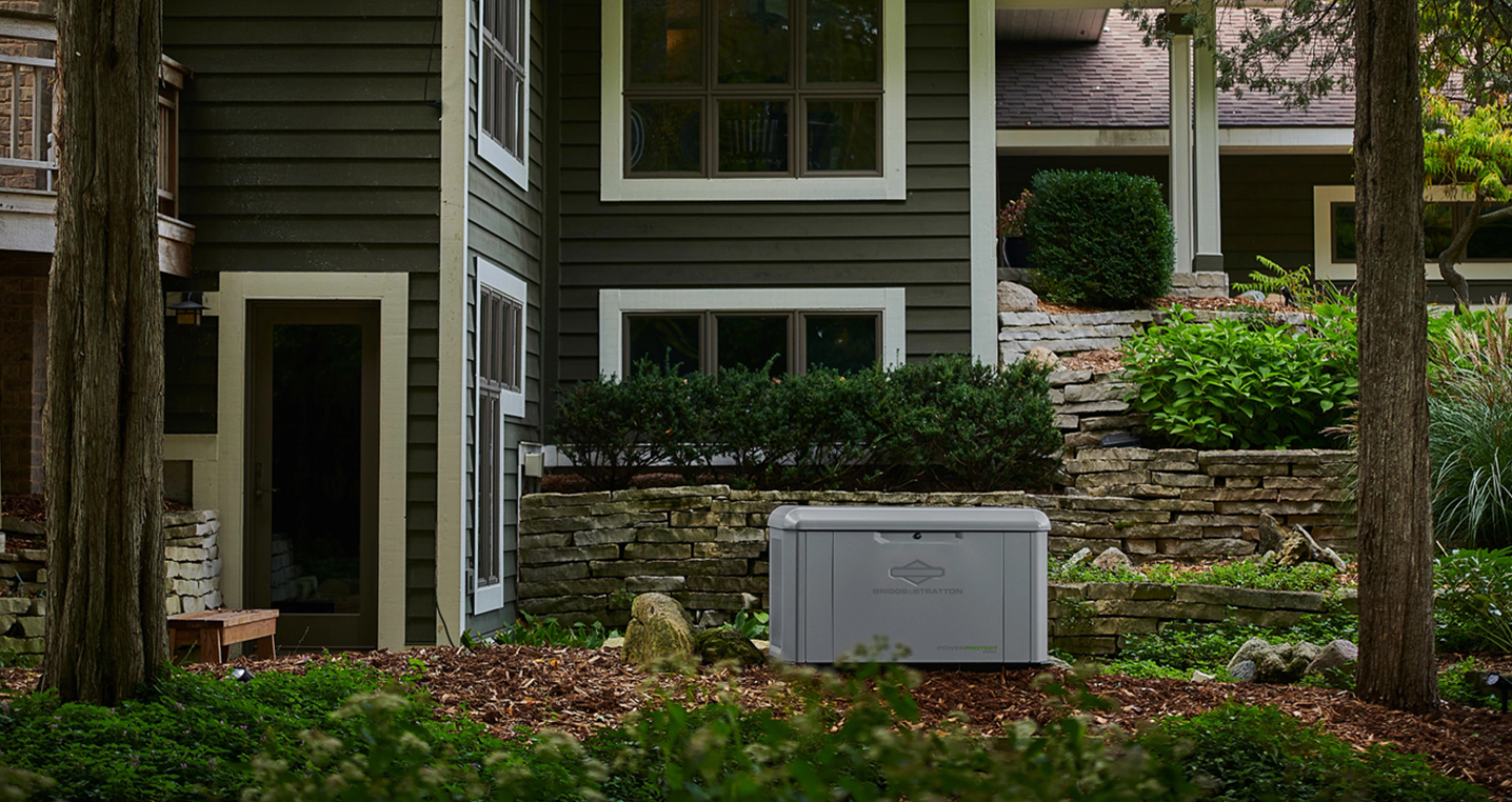 Front of a dark green house with white trim, stone foundation, and a gray utility box in the yard
