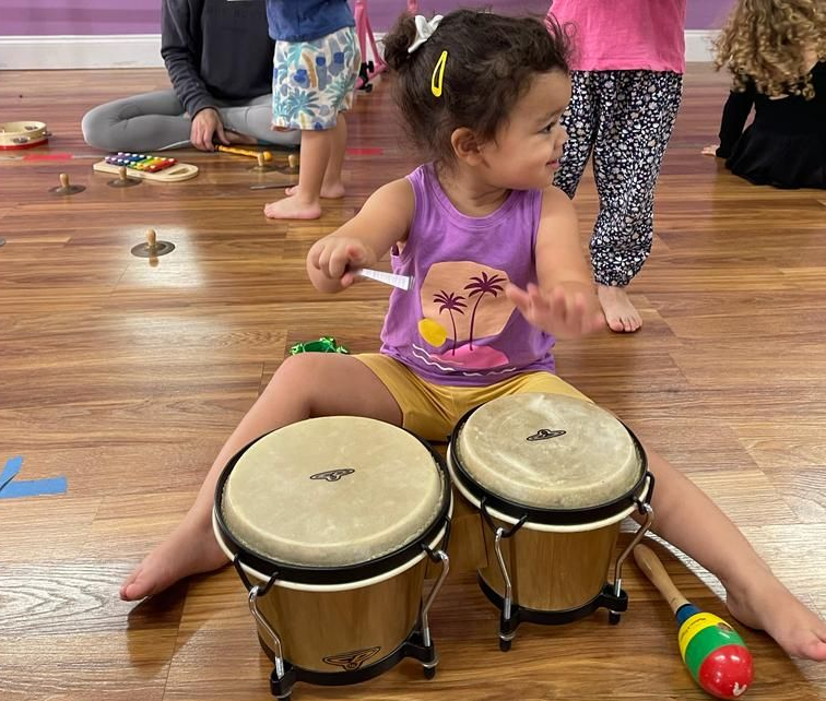 Child sitting on the floor playing bongos in a classroom or music room