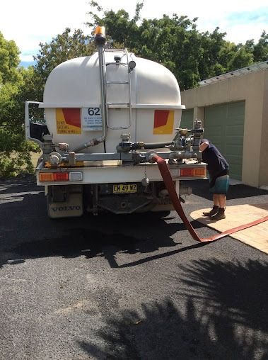 A Man Is Standing Next To A Large White Truck With A Hose Attached To It — Glass~a~Water In Eungella, NSW