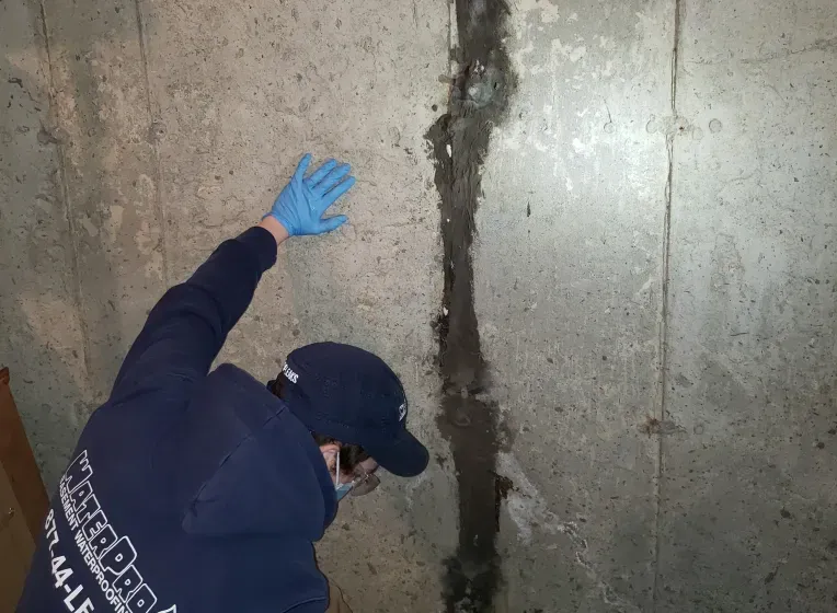 A man wearing blue gloves is standing in front of a concrete wall.