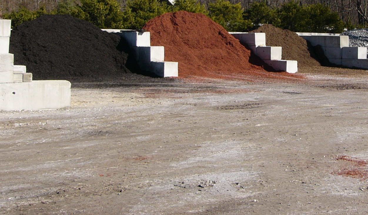 A row of piles of dirt are lined up in a parking lot.