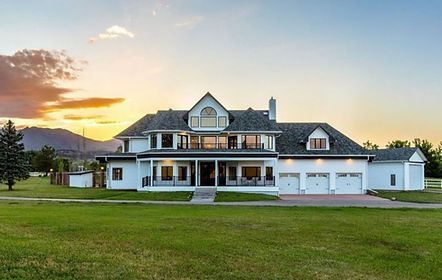 A large white house is sitting on top of a lush green field.