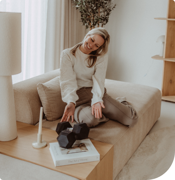 Woman sitting on a beige couch, leaning over a coffee table with a black geometric sculpture and books.