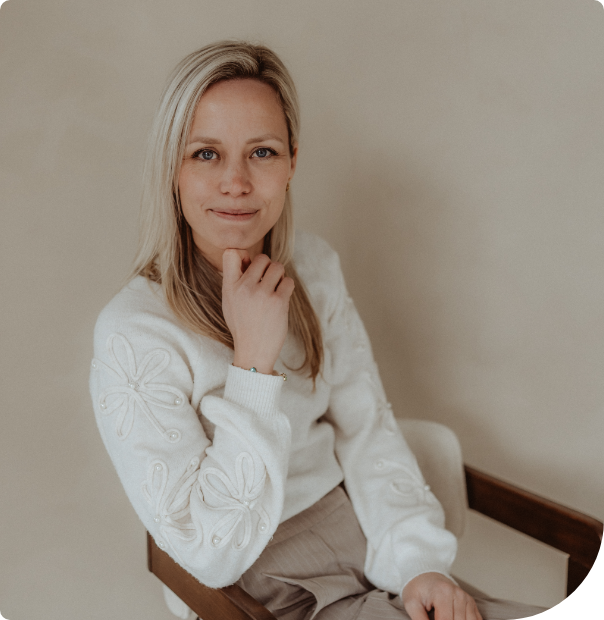 Woman in a white sweater seated on a chair, looking at the camera with a slight smile.