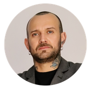 Retrato de um homem careca com barba e tatuagem no pescoço contra um fundo cinza claro.