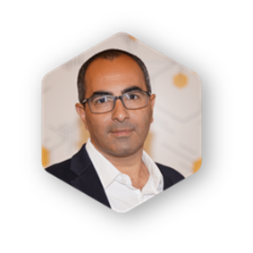 Man with glasses in a blazer and white shirt, set inside a white hexagonal shape.