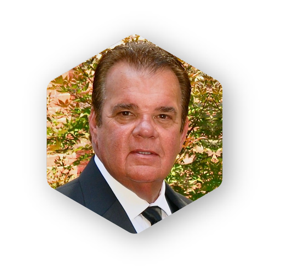 Man in a suit, looking at the viewer, set against a leafy background within a hexagon shape.