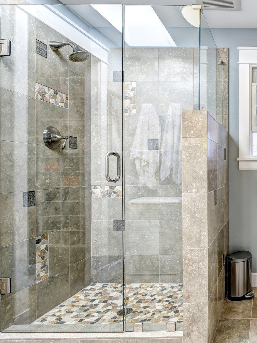 Glass walk-in shower with gray tile walls and a pebble mosaic floor in a modern bathroom