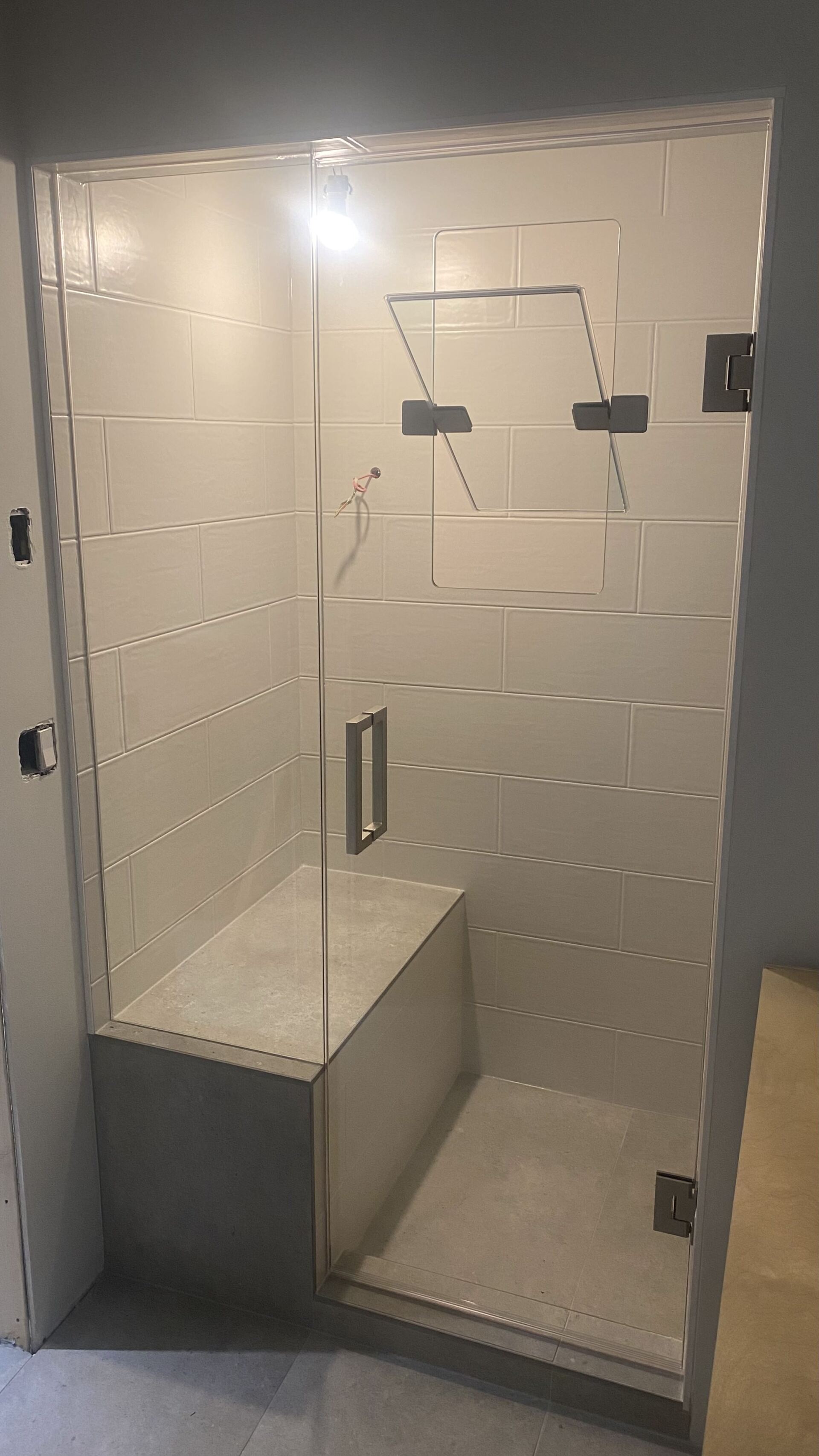 A bathroom with a walk in shower with a glass door and a bench.