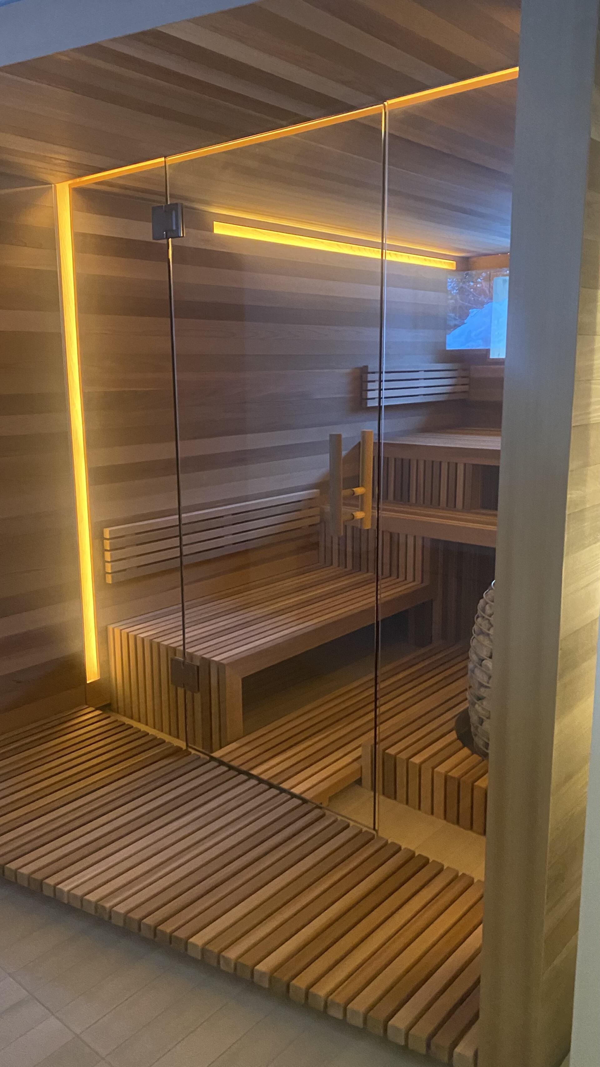 A wooden sauna with a glass door and wooden benches.