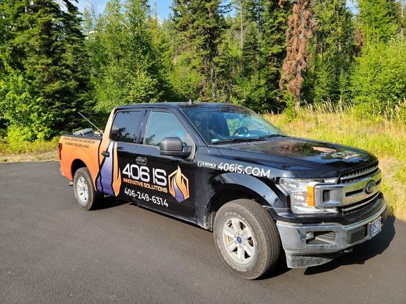 Black Ford F-150 truck with company logo parked on pavement, forest in the background.