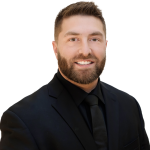 A man with a beard is wearing a suit and tie and smiling.
