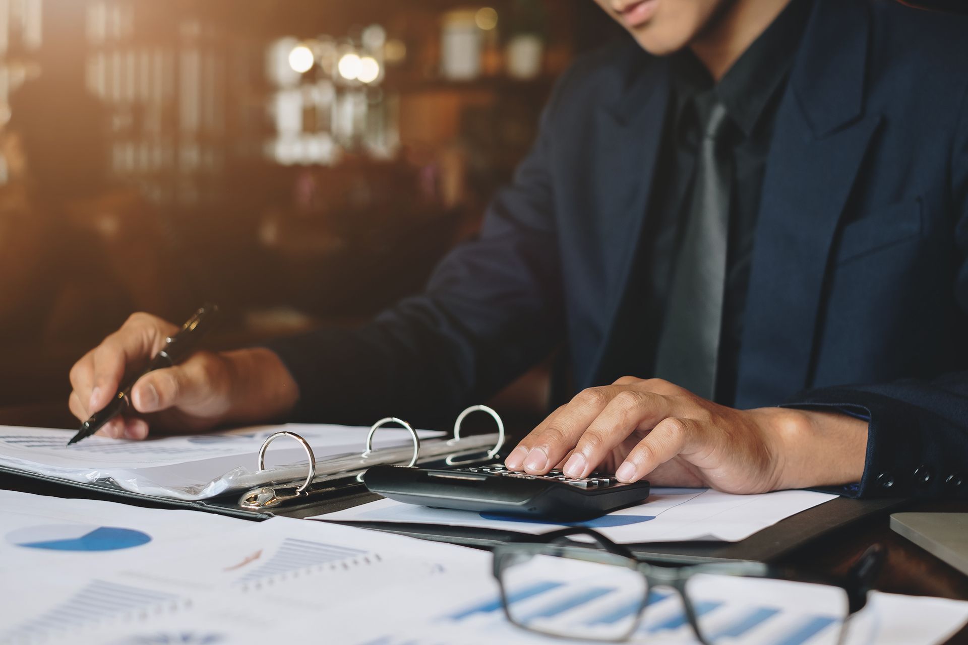 A Man is Sitting at a Table Using a Calculator and a Pen
