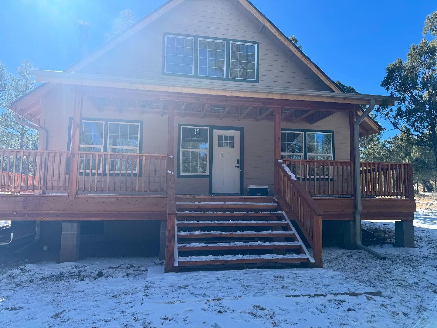 Front view of a cabin-style house with wooden porch, steps, and snow-covered ground