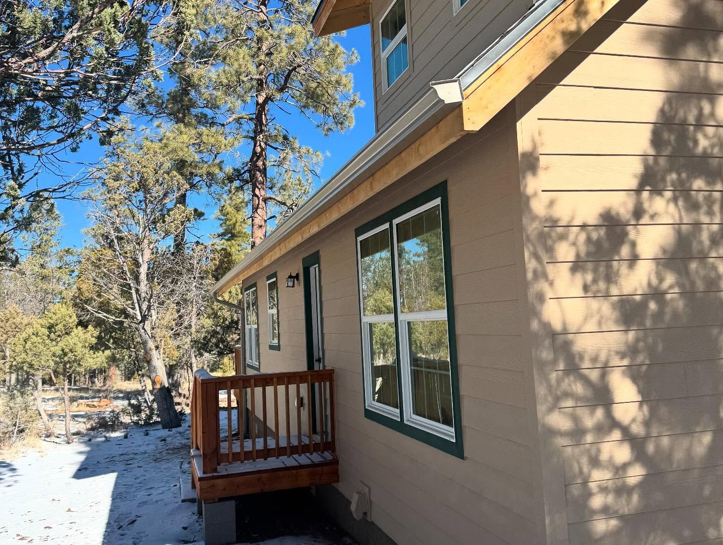 Tan house exterior with a small wooden porch, large windows, and snow along the side yard.