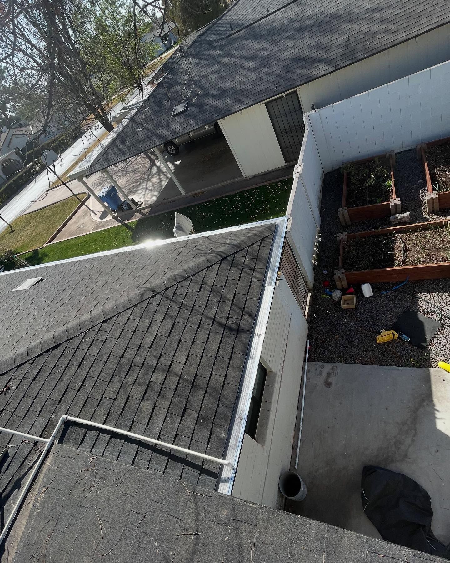Rooftop and narrow side yard between houses, with gray shingles, white walls, and a brick patio below.