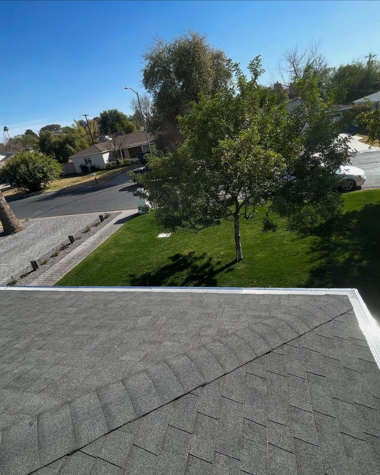 View from a rooftop over a green lawn, trees, and a quiet suburban street under a blue sky