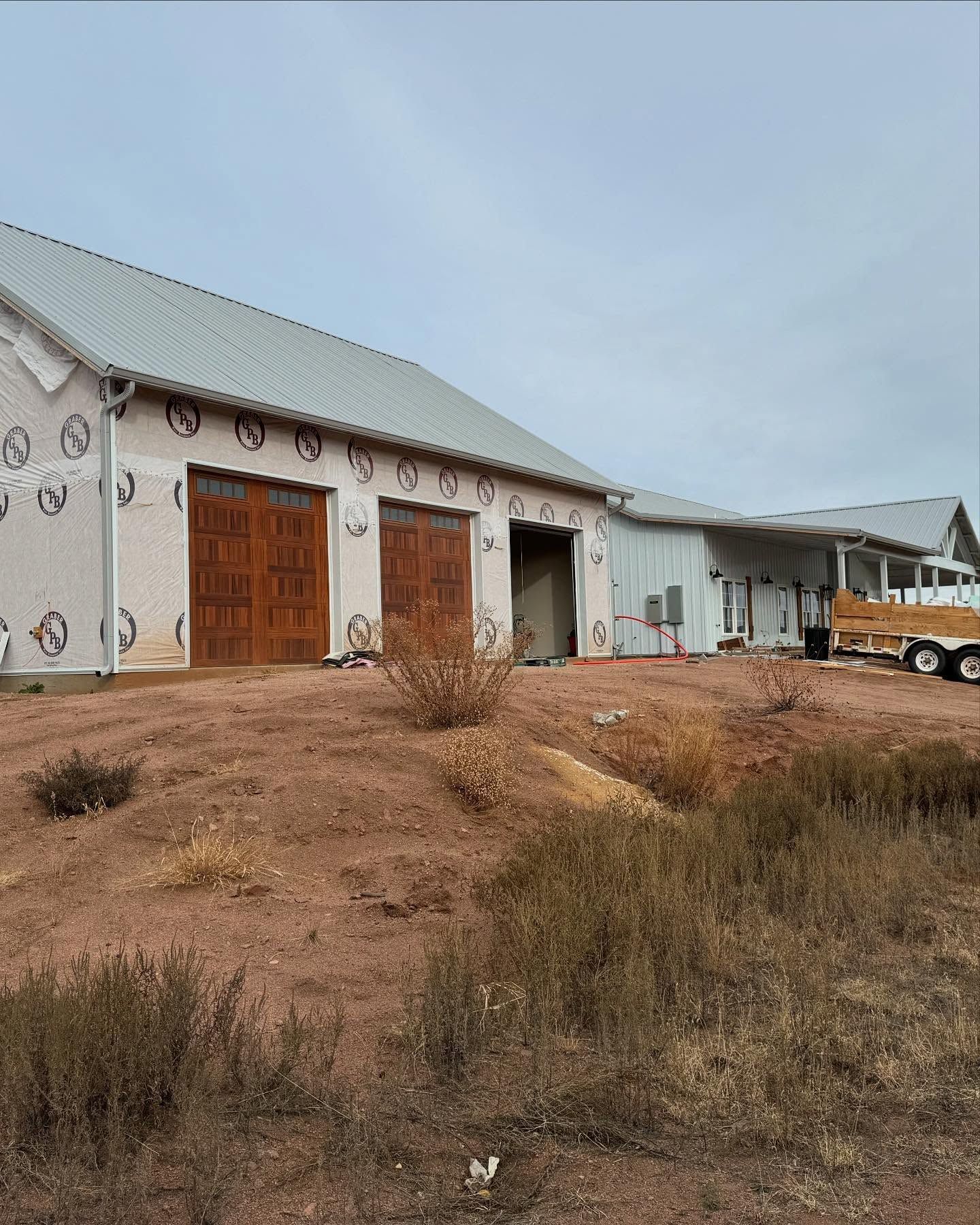 Rural barn with white siding and wooden doors, surrounded by dry grass under a cloudy sky.