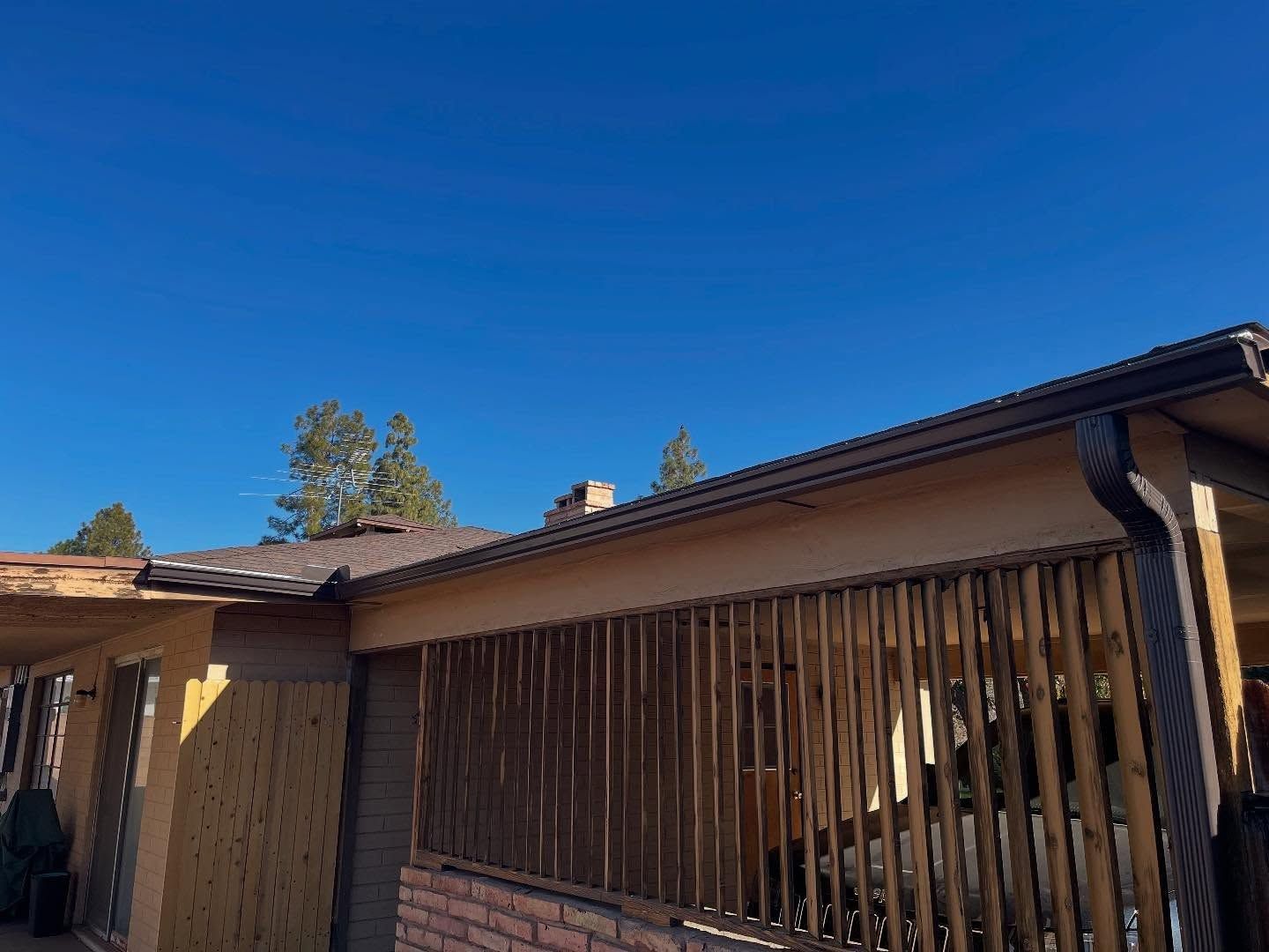 Single-story house exterior with brown roof and wooden fence under a clear blue sky
