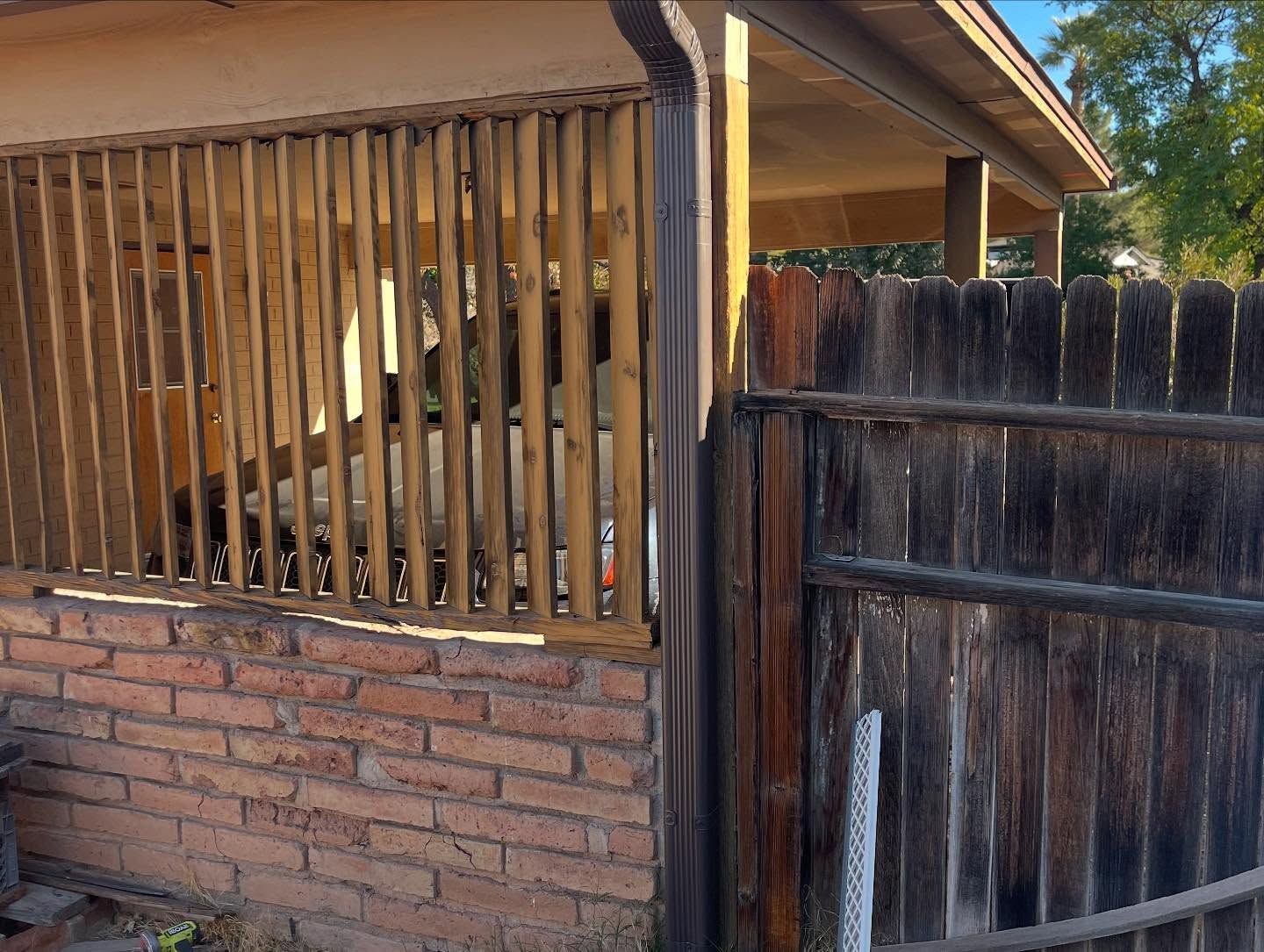 Wooden fence and brick wall beside a house porch, with a weathered gate on the right.