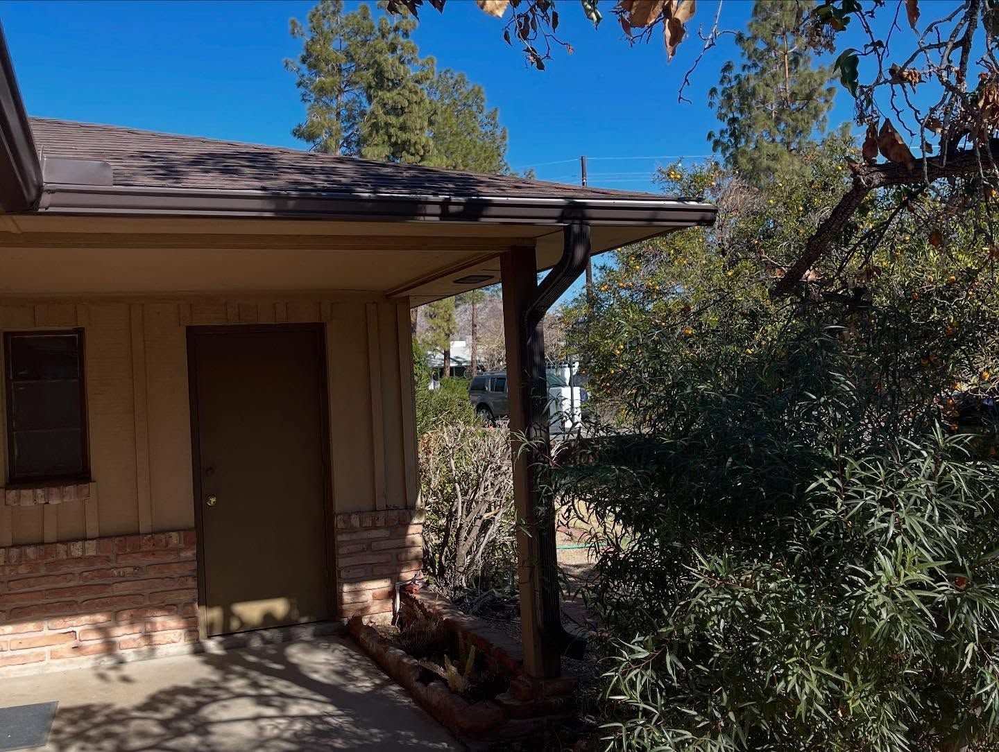 Front porch of a house with a brown door, brick siding, and trees casting shade.