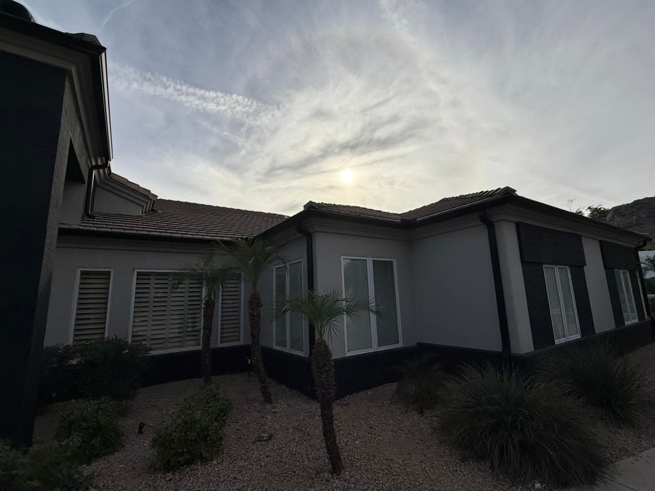 Exterior of a white stucco house with dark roof tiles and shuttered windows under a cloudy sky