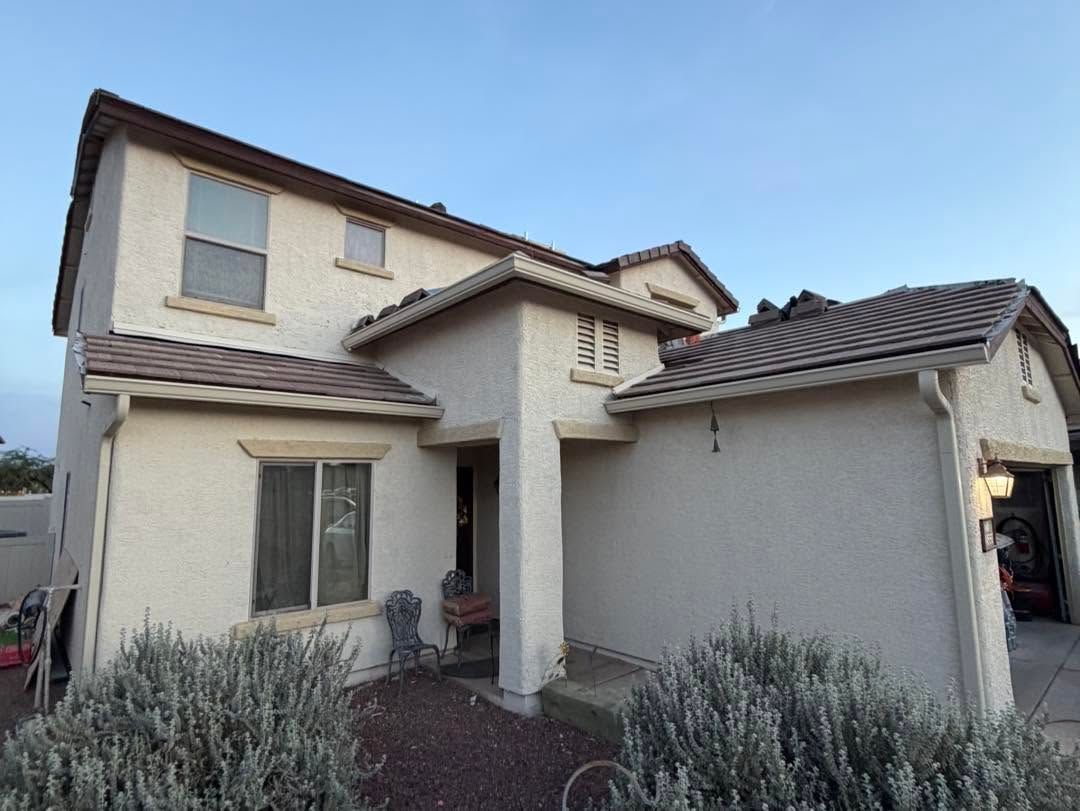 Two-story beige stucco house with tiled roof and a garage under a blue sky