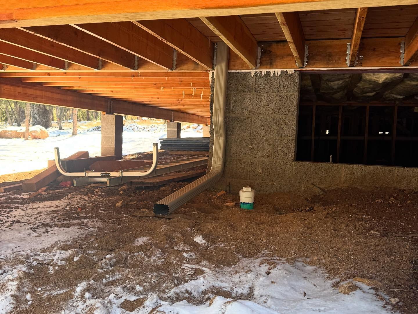 Covered outdoor walkway with exposed beams, gravel ground, and patches of snow beside a building