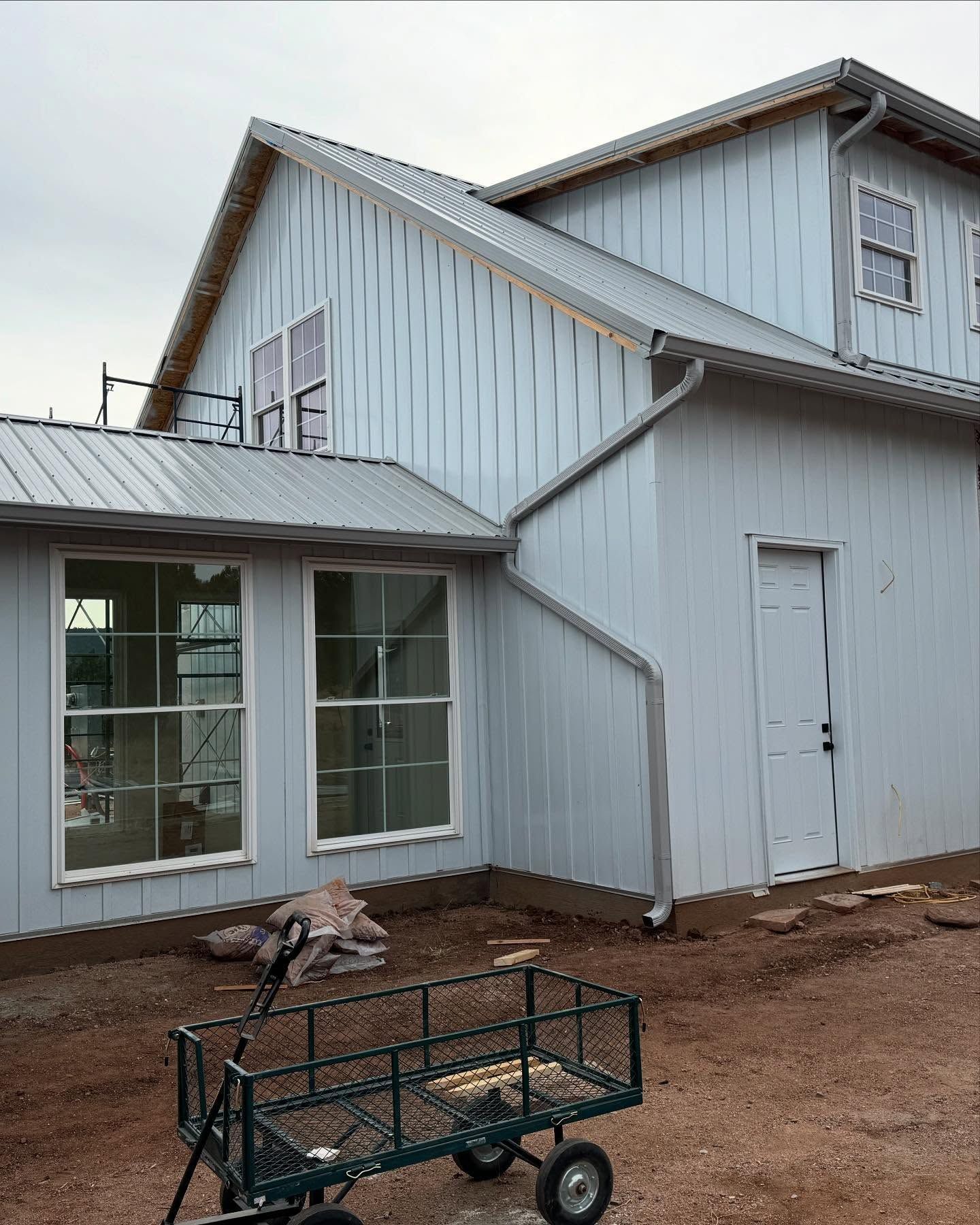 White two-story house exterior with windows, a side door, and a gravel yard with a small cart in front