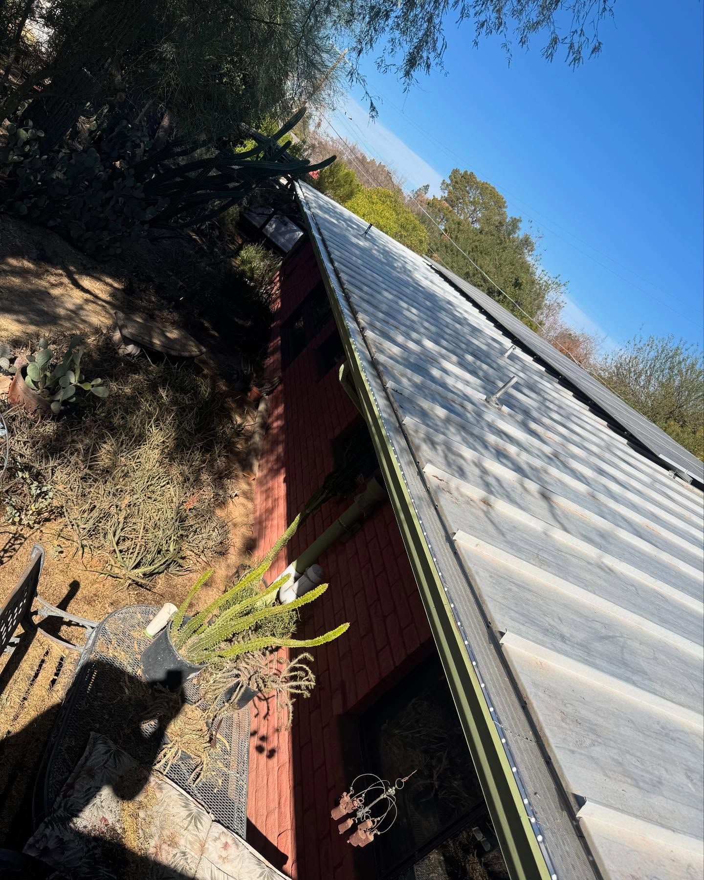 Tilted view of a metal-roofed red building with trees and a bright blue sky nearby