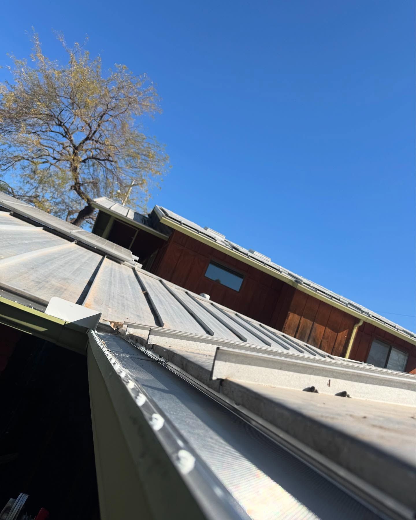 Steep metal roof leading up to a red house under a clear blue sky, with a tree in the background