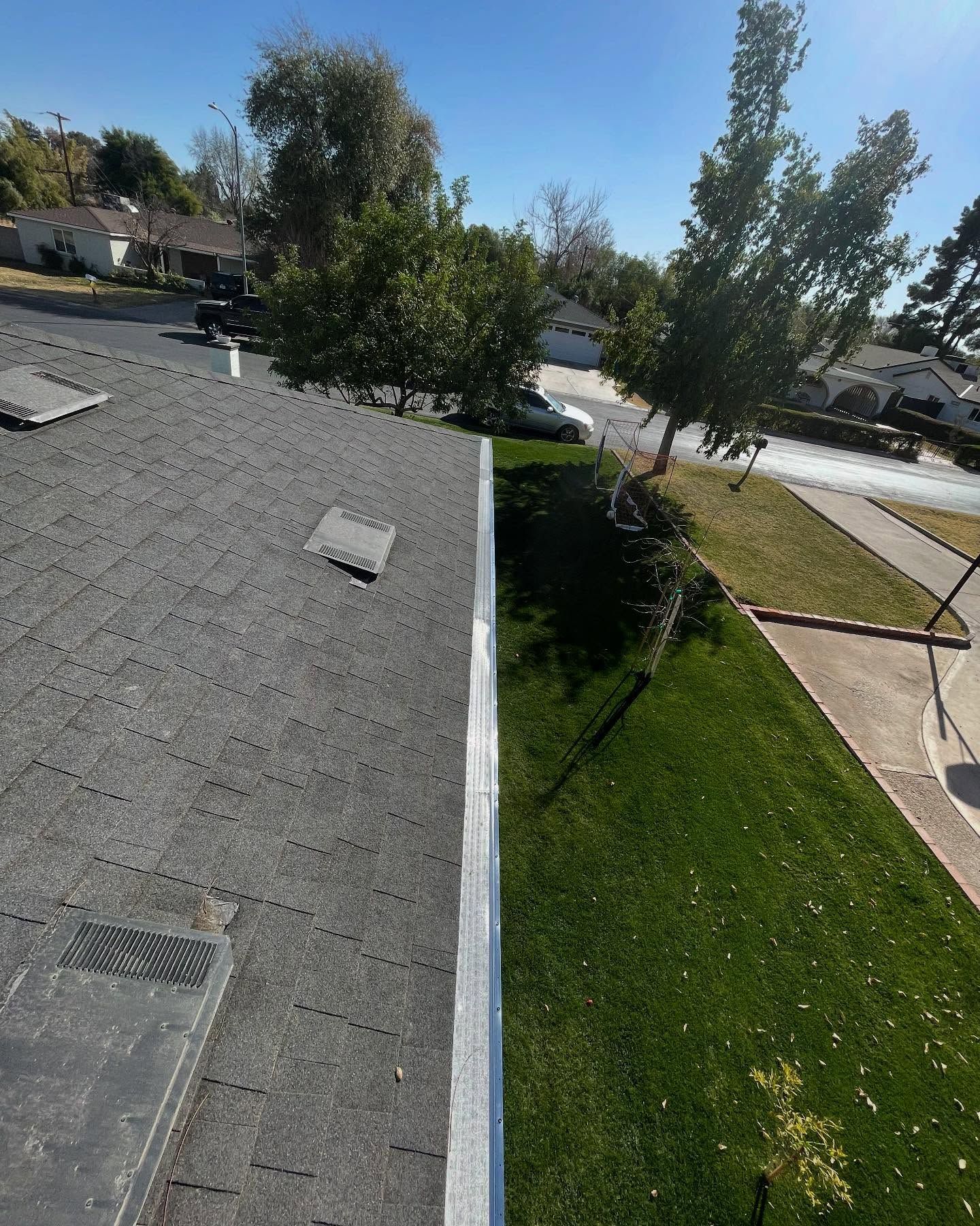 Rooftop view of a suburban street with trees, lawn, and neighboring houses under a clear blue sky