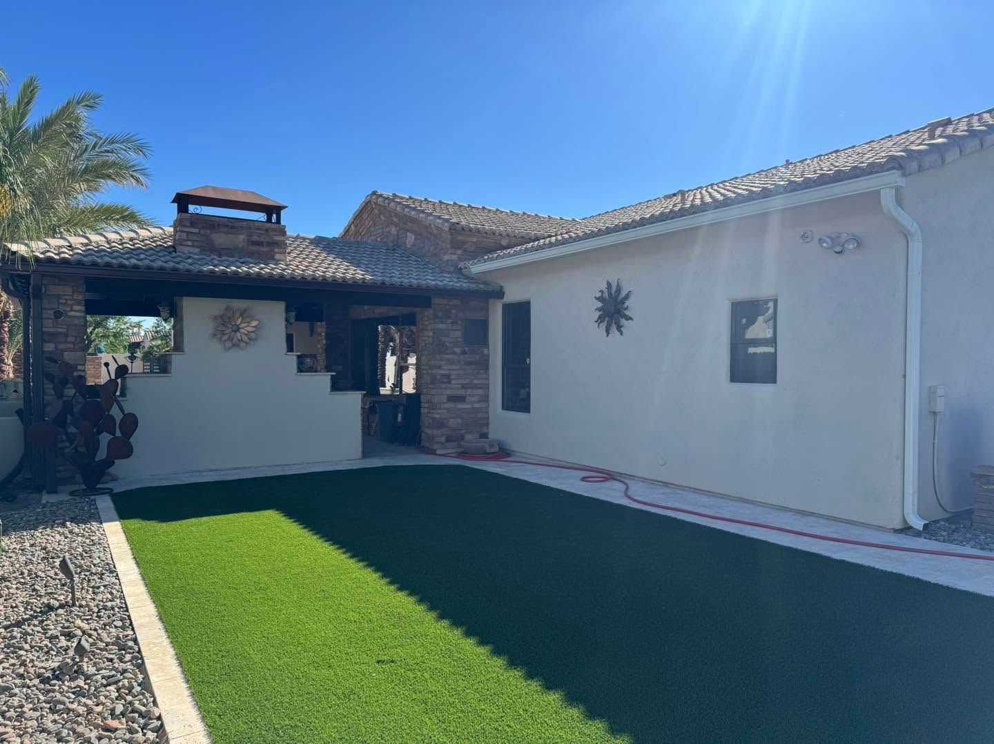 Sunlit courtyard with artificial grass, white stucco walls, and a tiled roof under a clear blue sky