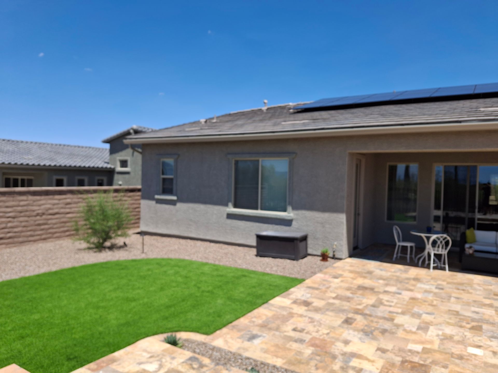 Backyard patio with pavers, green lawn, and a stucco house exterior under a clear sky
