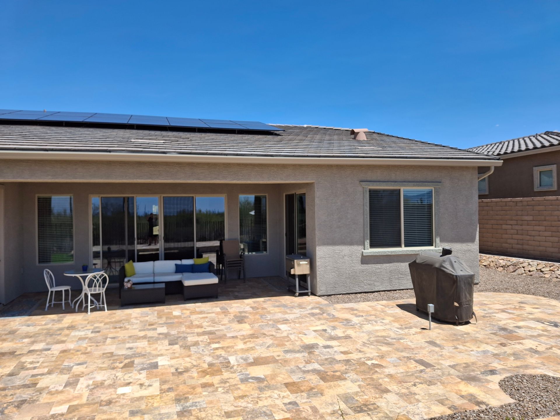 Patio with brick pavers, outdoor seating, grill, and sliding doors under a blue sky