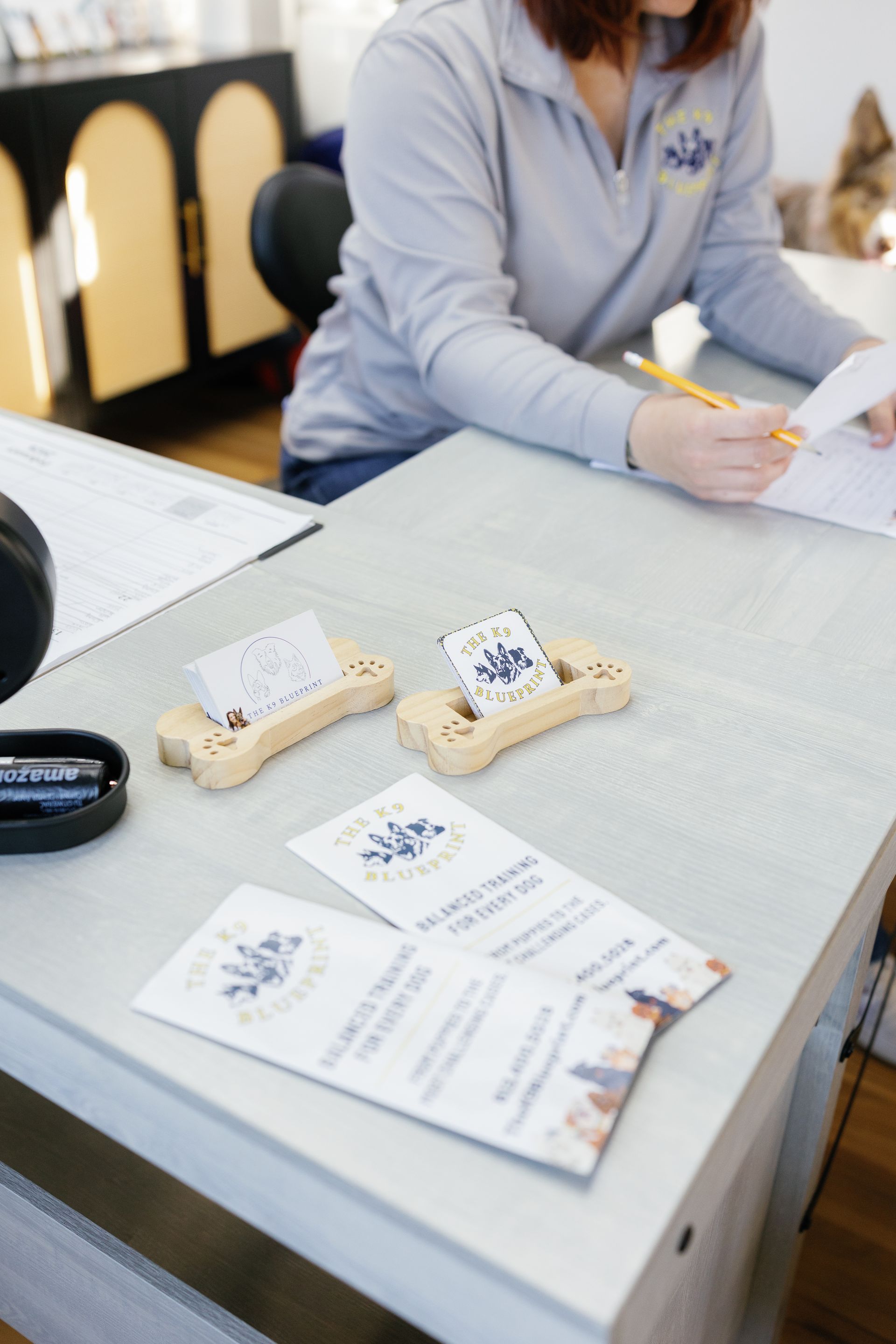 Person writing at a table with brochures and small wooden objects displayed.