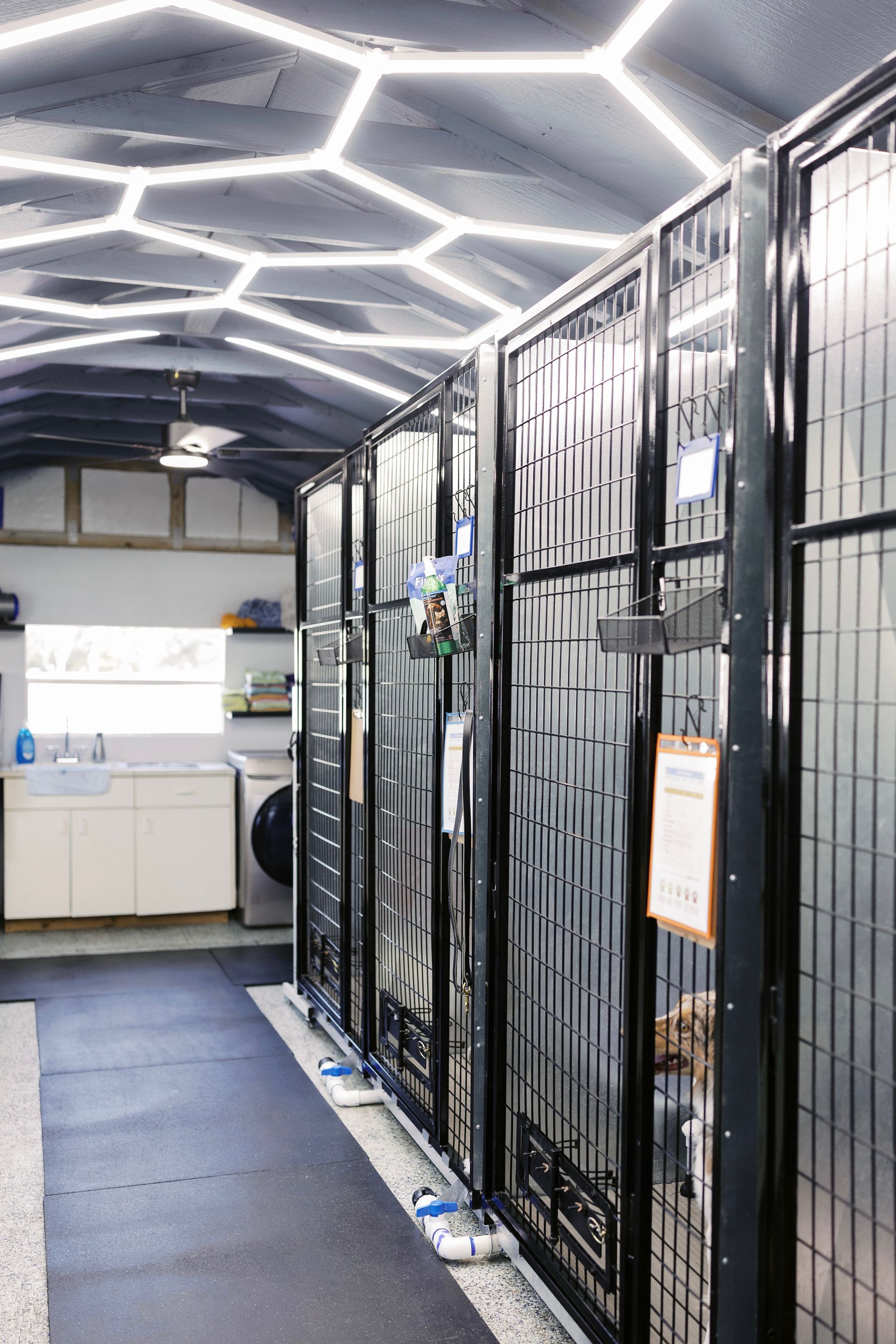 Server room with tall black equipment racks, lit by hexagonal ceiling lights, and a small sink area at the far end