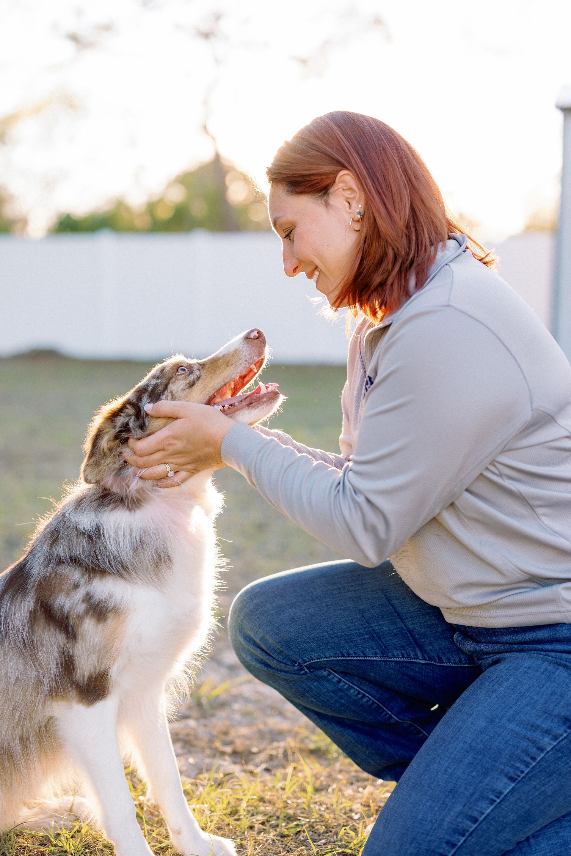 Woman kneeling outdoors petting a happy dog by the water at sunset
