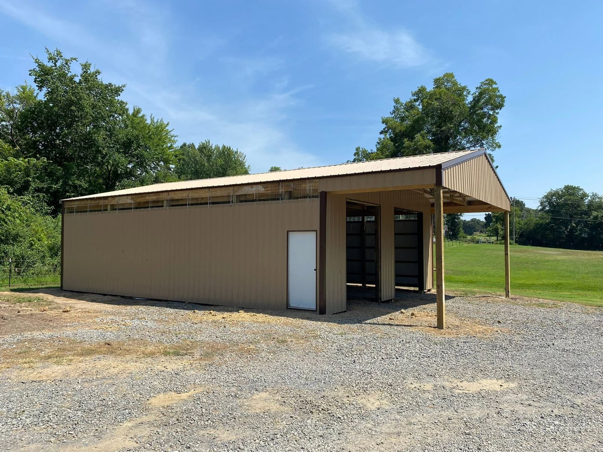 Small tan metal shed with open front in a gravel lot under a blue sky.