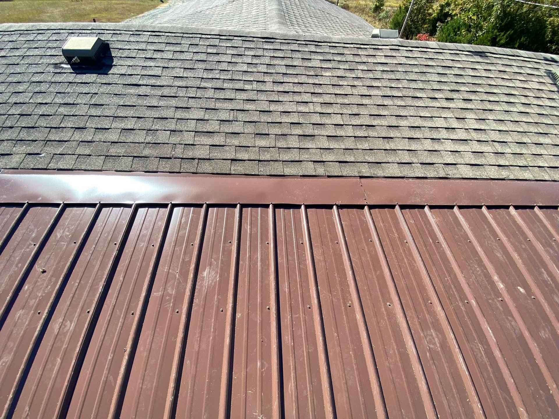 Rooftop with brown metal awning below gray shingle roof and a small vent on the left