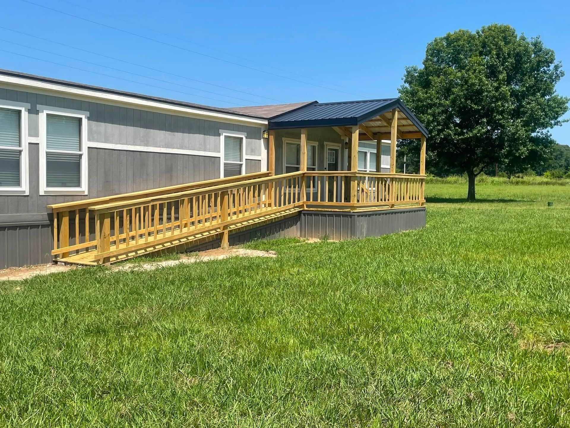 Wooden ramp and deck entrance on a gray building beside a grassy yard under a blue sky