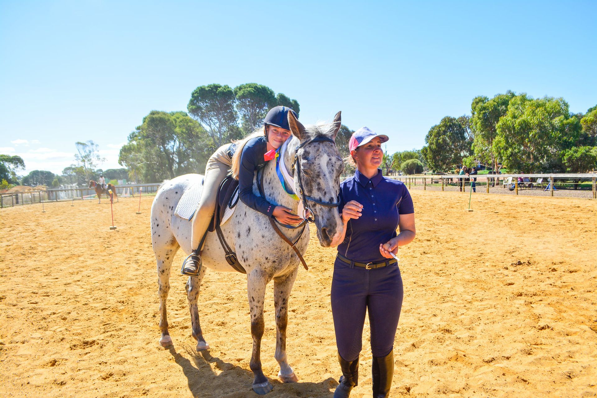 riding student hugging a horse in the outdoor arena with an instructor