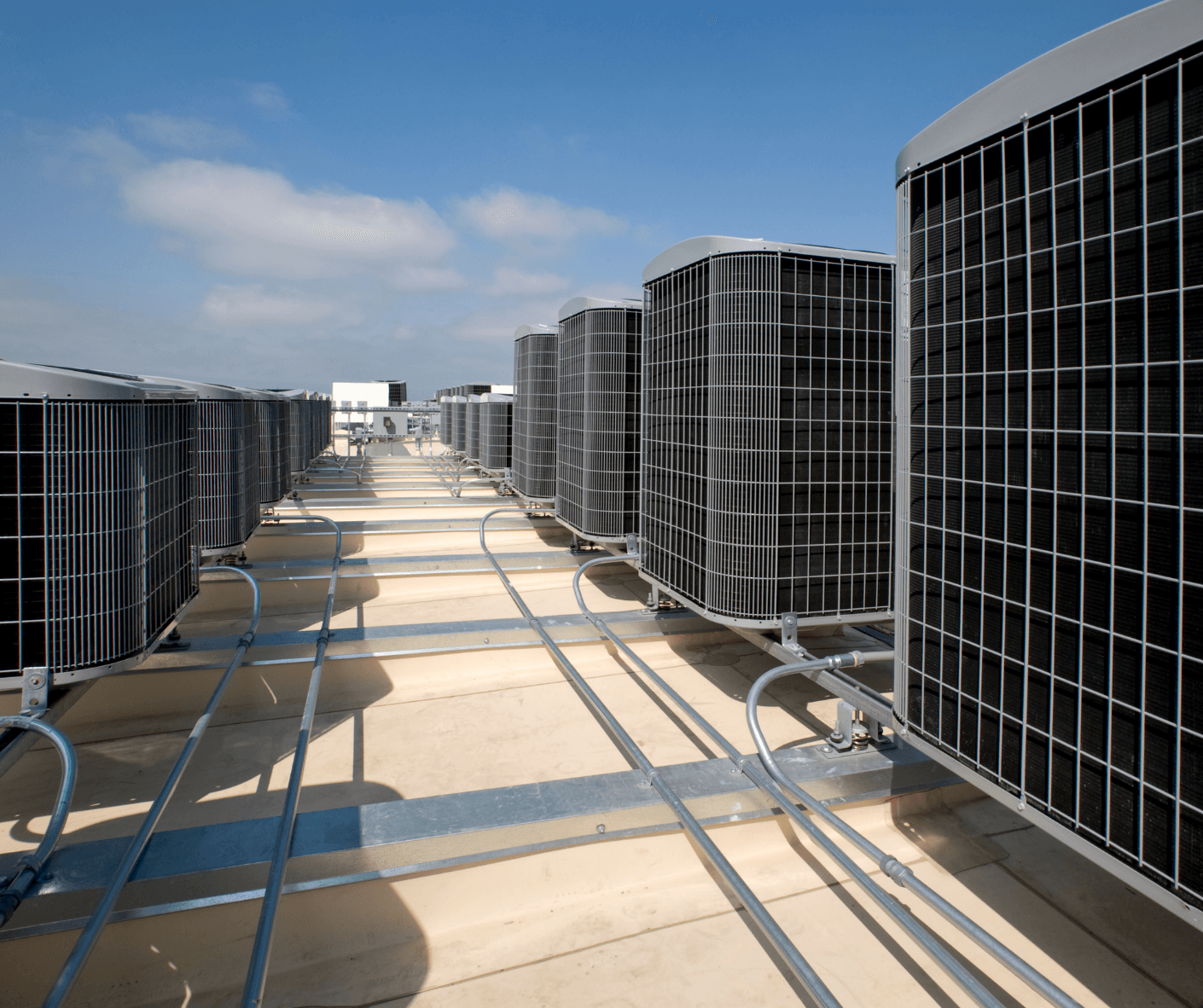 Rows of large rooftop HVAC units on a concrete commercial roof under a blue sky