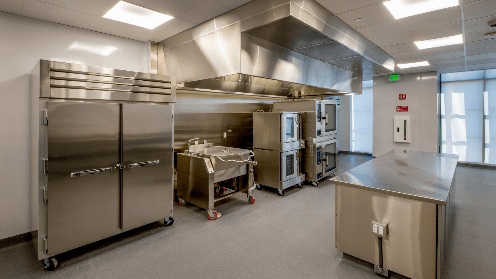 Commercial kitchen with stainless steel appliances, prep tables, and bright overhead lighting