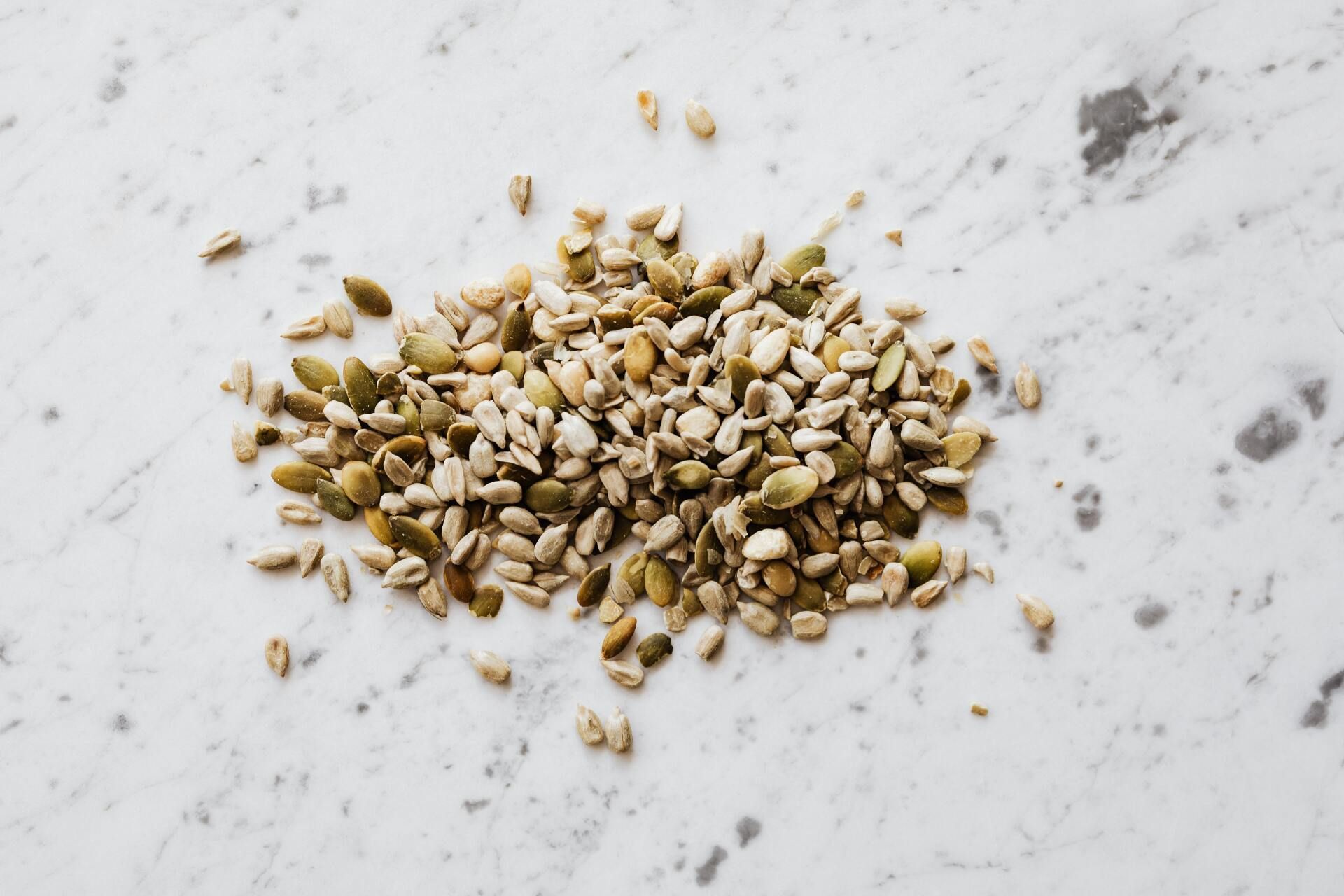 A pile of sunflower seeds and pumpkin seeds on a white surface.